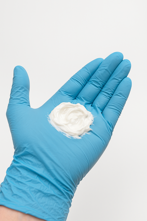 Blue glove holding Neuro Med BLT Cream against a light gray background