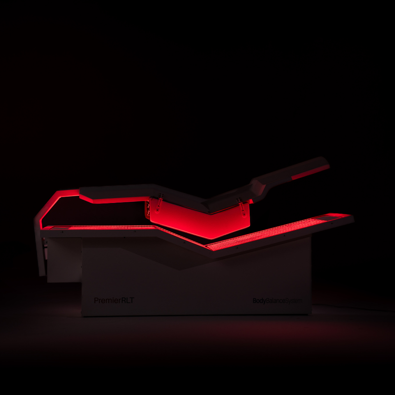 Body Balance System Premier RLT red light therapy bed on a black background with lights on