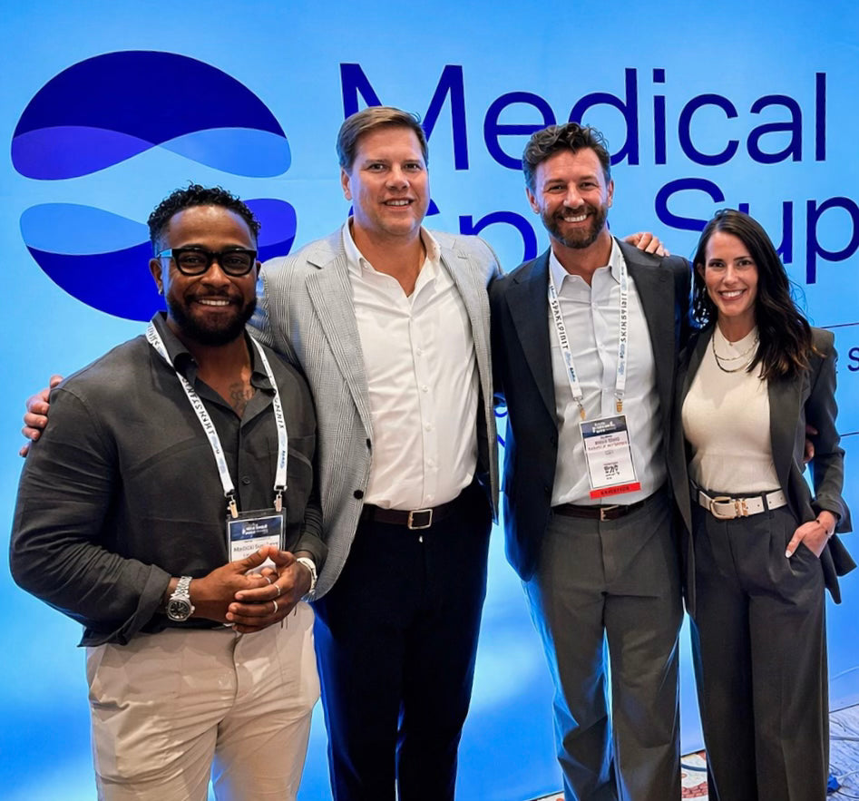 Four professionals posing together in front of a 'Medical Supply' backdrop